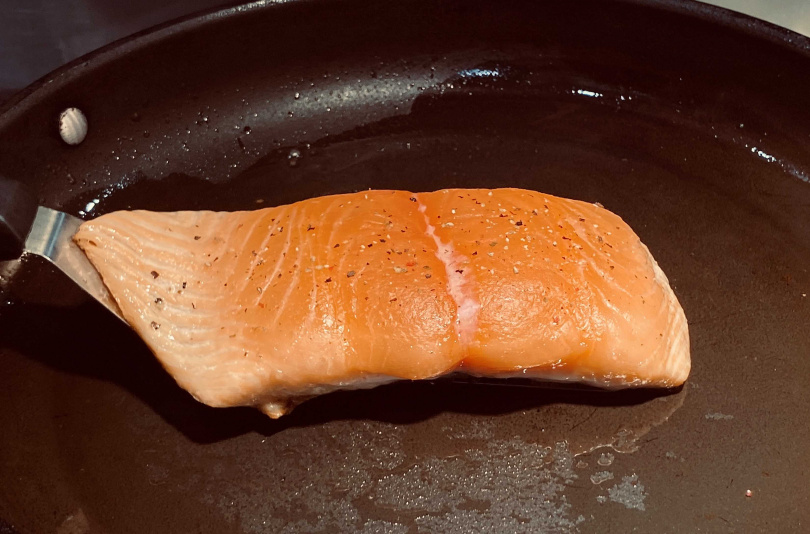 4.在中小火的狀態下，鮭魚肉正被慢慢加溫，從側面觀察，看到魚肉慢慢熟至約有8成、變成白色的狀態才可翻面。