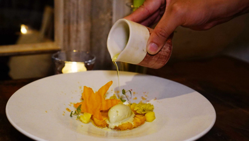 甜點「金鑽鳳梨 鹹蛋黃 甜玉米」上桌時淋上白蘭地冷露與無花果葉油，一旁則是以地瓜製成的楓葉。（圖／魏妤靜攝）