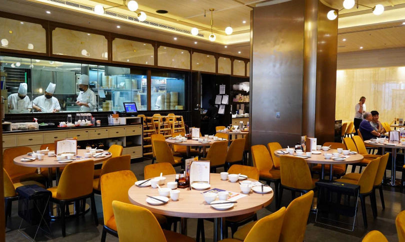 新店裝的餐椅繃布與腰牆磁磚的「鵝黃棕」選色靈感取自品牌的八色小籠包，並可透過半開放式廚房看師傅展演。