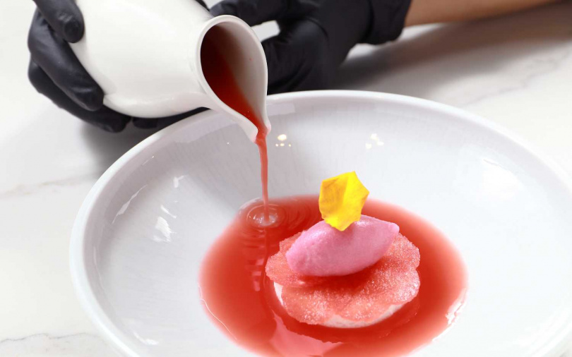 「華寶西瓜／荔枝／玫瑰」上桌時會緩緩注入西瓜冷湯，讓整道甜點呈現像是盛夏綻放的荷花美景，從視覺到味覺都暑氣全消。（圖／趙文彬攝）
